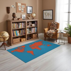 Puede incluir: Una alfombra rectangular azul con un diseño de mapa del mundo en naranja. La alfombra está colocada sobre un suelo de madera clara en una habitación con una estantería, un sillón y un globo terráqueo.