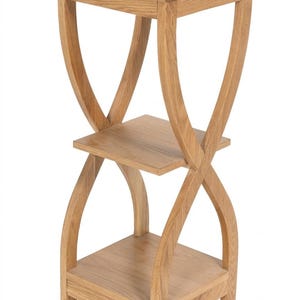 May include: A light brown wooden stand featuring three square shelves arranged vertically. The structure is supported by four curved, intersecting legs that create an hourglass shape, connecting the top, middle, and bottom tiers together.