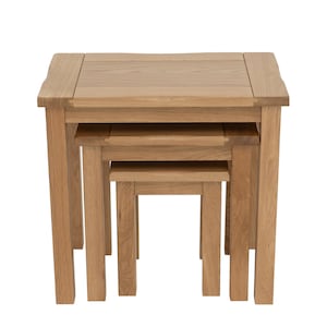 May include: A set of three light brown wooden nesting tables with a natural grain finish. The tables are stacked together, featuring square tops and four straight legs each, with the largest table on the outside and the smallest in the centre.