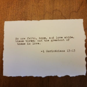 Könnte beinhalten: Eine weiße Karte mit schwarzem Text, der lautet: "So now faith, hope, and love abide, these three; but the greatest of these is love. -1 Corinthians 13:13"