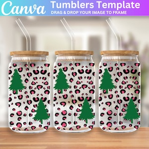 May include: Three clear glass tumblers with wooden lids and pink and black leopard print designs with green Christmas trees. Each tumbler has a clear plastic straw.