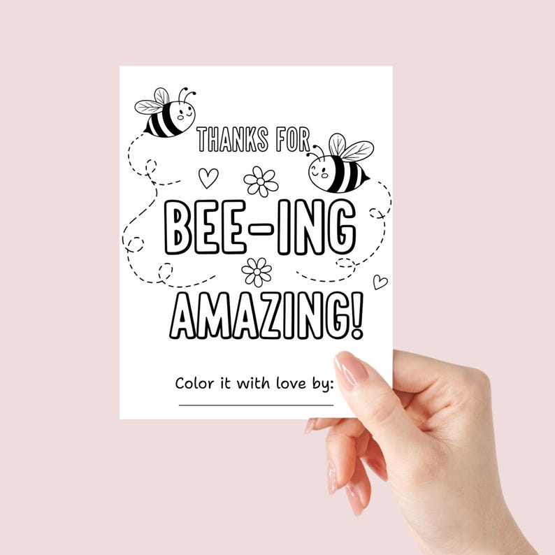 May include: A white card with the text "THANKS FOR BEE-ING AMAZING!" in black, along with illustrations of bees, hearts, and flowers. The card is held by a hand against a light pink background. The bottom of the card reads "Color it with love by:"