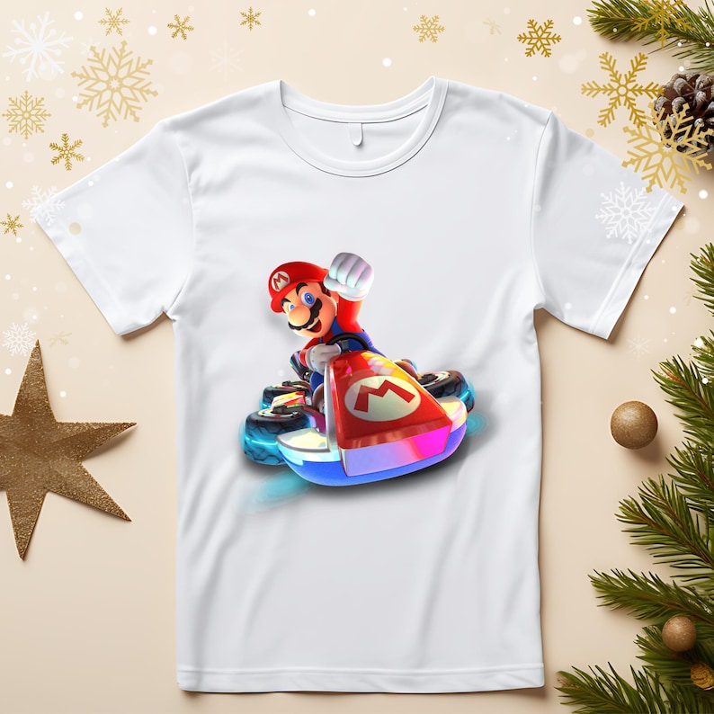May include: White t-shirt featuring a colorful graphic of Mario in a kart. The kart has a red and white front with the letter "M". Mario is wearing his signature red hat and blue overalls. The design is vibrant and eye-catching.