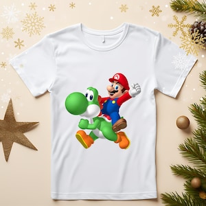 May include: White t-shirt featuring a colorful graphic of Mario riding Yoshi. Mario is wearing a red hat, blue overalls, and a red shirt. Yoshi is green with orange shoes. The design is centered on the shirt.