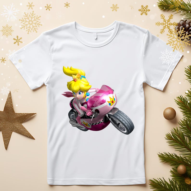 May include: White t-shirt featuring a cartoon character riding a pink motorcycle. The character has blonde hair and is wearing a pink outfit. The motorcycle has a checkered pattern and a gold crown design.