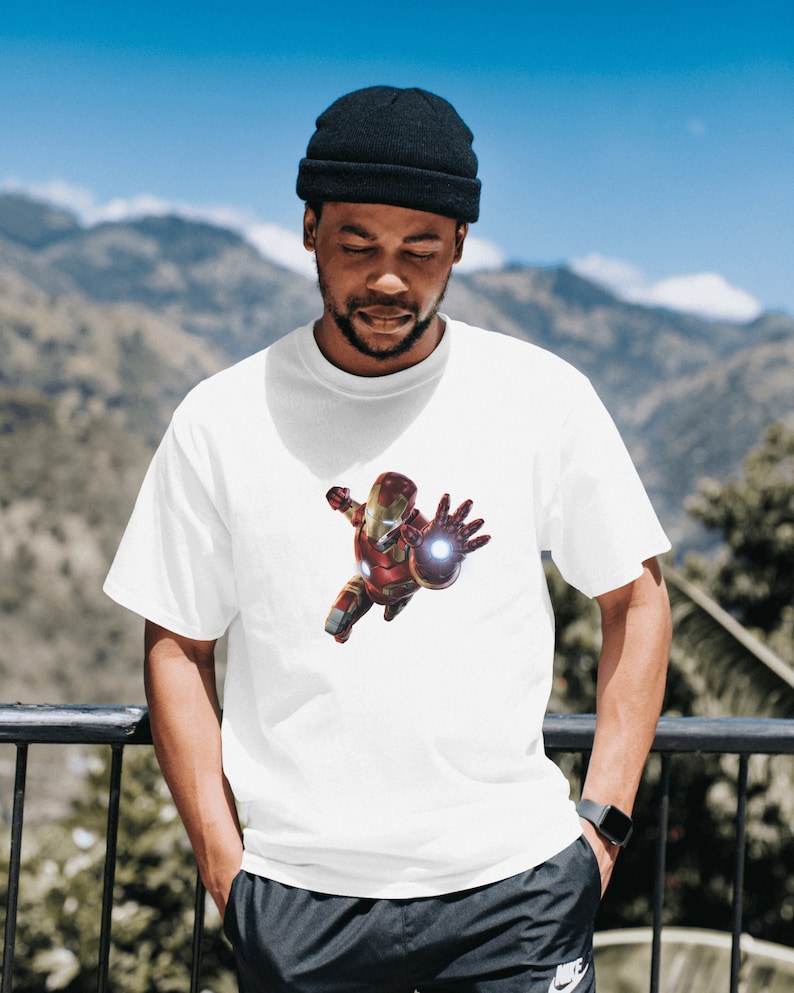 K&ouml;nnte beinhalten: Ein wei&szlig;es T-Shirt mit einem roten und goldenen Iron Man-Motiv auf der Vorderseite. Das Motiv zeigt Iron Man im Flug mit ausgestreckter Hand, der einen Repulsorstrahl abfeuert.