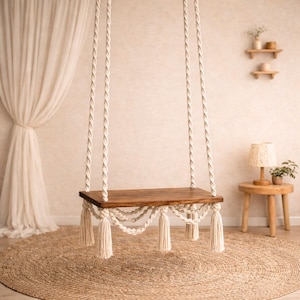 May include: A rectangular wooden swing seat suspended by thick, twisted off-white cotton ropes. The seat features decorative macrame knotting along the front edge, finished with long, dangling tassels at each corner and along the bottom edge.