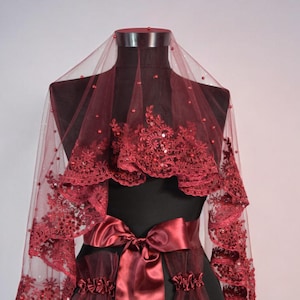 May include: A burgundy bridal veil with a satin ribbon and lace trim. The veil is displayed on a mannequin.