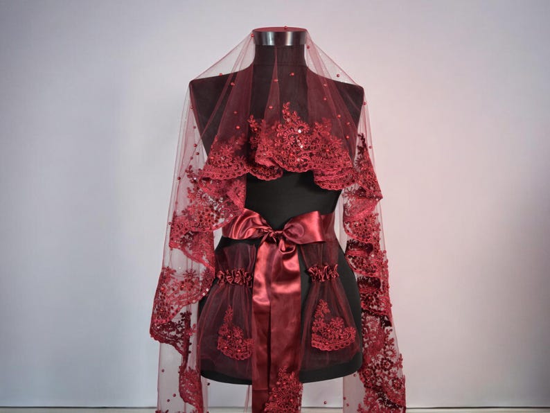 May include: A burgundy bridal veil with a satin ribbon and lace trim. The veil is displayed on a mannequin.