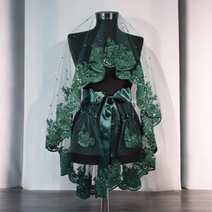 May include: A green tulle veil with lace trim and a satin ribbon. The veil is on a mannequin and has a scalloped edge.
