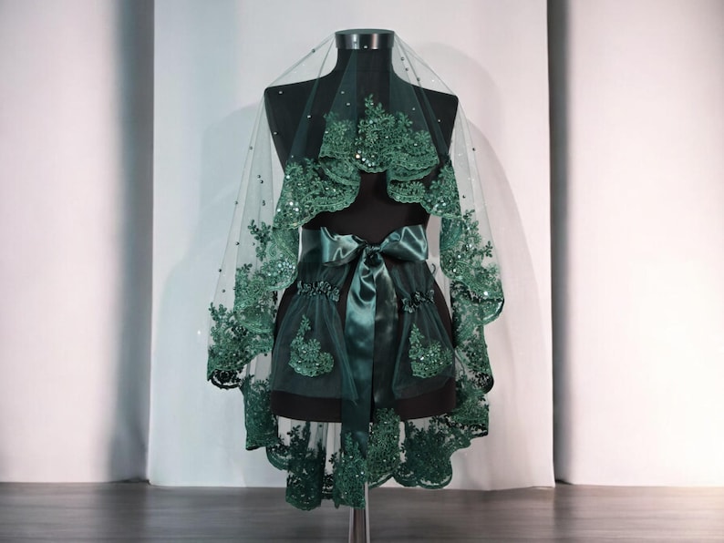 May include: A green tulle veil with lace trim and a satin ribbon. The veil is on a mannequin and has a scalloped edge.