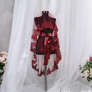May include: A burgundy lace bridal veil with a satin ribbon and beaded embellishments. The veil is displayed on a mannequin against a white backdrop.