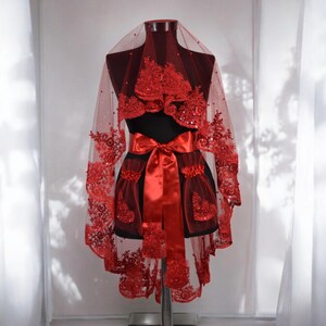 May include: A red bridal veil with lace and sequins. The veil is trimmed with a red satin ribbon and has a heart-shaped design.