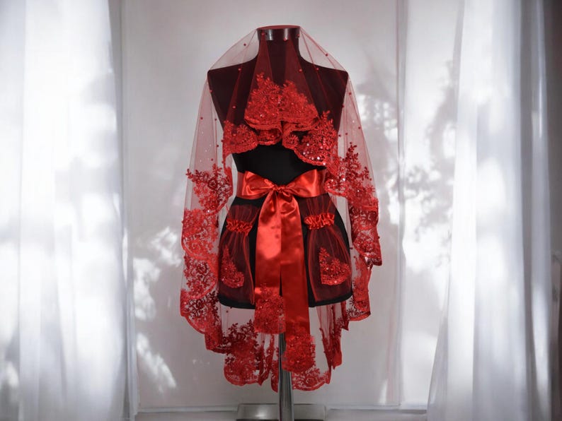 May include: A red bridal veil with lace and sequins. The veil is trimmed with a red satin ribbon and has a heart-shaped design.