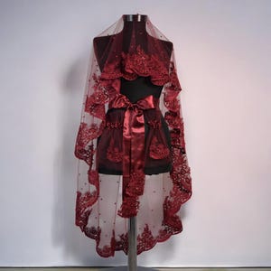 May include: A burgundy bridal veil with a satin ribbon and beaded lace trim. The veil is displayed on a mannequin.
