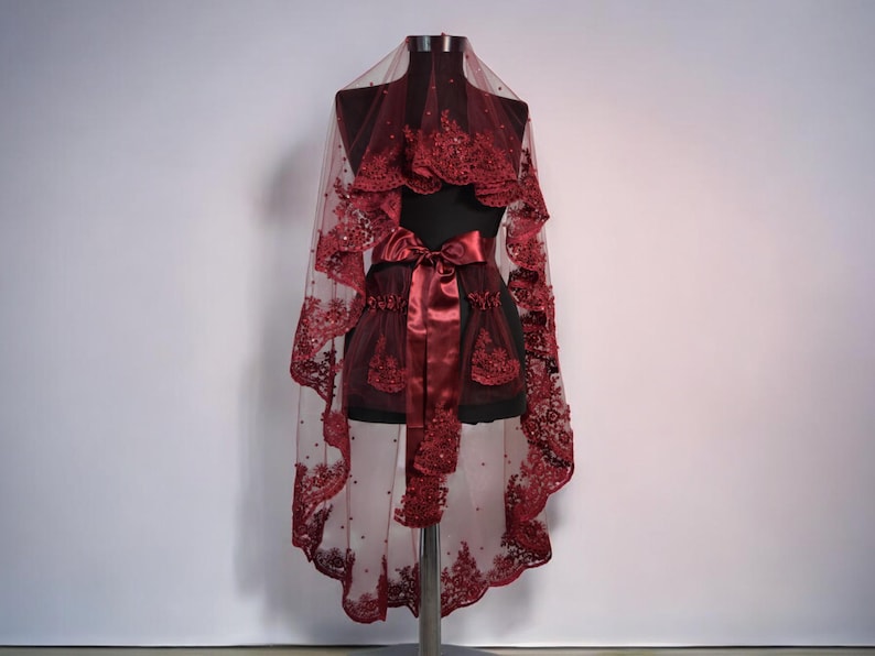 May include: A burgundy bridal veil with a satin ribbon and beaded lace trim. The veil is displayed on a mannequin.