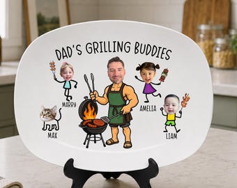 May include: White oval ceramic platter with the text "Dad's Grilling Buddies" and cartoon illustrations of a man grilling, three children, and a cat. The platter is displayed on a black stand.