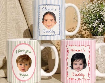 May include: Three white ceramic mugs with personalized photos and text. One mug has blue stripes with a photo of a girl and the text "Olivia's Daddy". Another has pink stripes with a photo and the text "Hanna's Daddy". The third mug has green stripes with a photo and the text "I love you Papa".