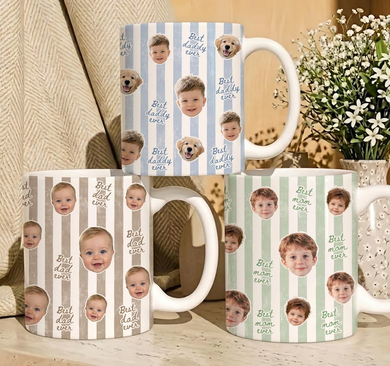 May include: Three ceramic mugs with white handles. One mug has blue and white stripes with baby faces and dog stickers, and the text "Best daddy ever". Another mug has brown and white stripes with baby faces and the text "Best dad ever". The third mug has green and white stripes with baby faces and the text "Best mom ever".