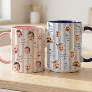 May include: Two ceramic mugs with personalized designs. One mug features a pink handle and interior with a pattern of baby faces and the text "Best grandma ever." The other mug has a blue handle and interior, with baby faces, puppies, and the text "Best mama ever."