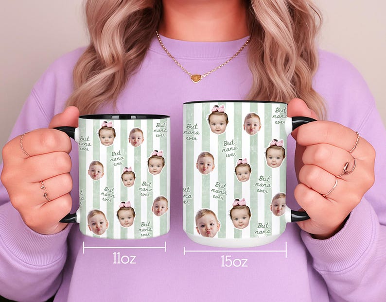 May include: Two white ceramic mugs with black handles and rims. The mugs feature a repeating pattern of baby faces and the text "Best Nana Ever" on a light green striped background. One mug is 11oz, the other is 15oz.