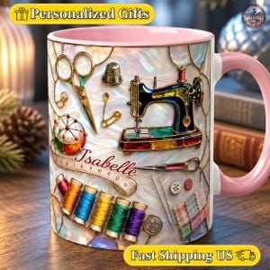 Puede incluir: Una taza de cerámica con asa e interior rosa, con una ilustración estilo vidriera de herramientas de costura que incluye una máquina de coser, tijeras, dedal, alfiletero, carretes de hilo y una cinta métrica con el nombre Isabelle.