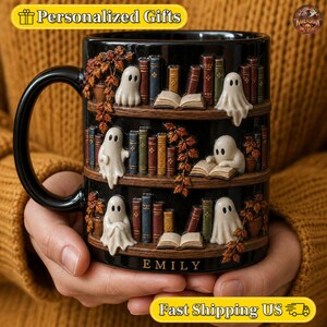 Peut inclure: Un mug en céramique noire orné d'étagères à trois niveaux avec des fantômes blancs, des livres miniatures colorés et des feuilles d'automne. Le prénom EMILY est inscrit en lettres dorées à la base du mug, doté d'une anse incurvée.