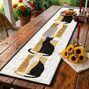 May include: A rectangular quilted table runner featuring a repeating pattern of stylized cats in black, white, and gray, each positioned on a gold-toned geometric rectangular background. The runner has a white background with a circular stitched texture.