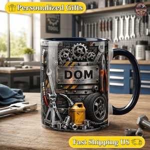 Peut inclure: Un mug en céramique avec un intérieur et une anse bleu foncé, orné d'un motif graphique représentant un atelier mécanique avec des engrenages, des clés, un pneu, un bidon d'huile jaune et une plaque métallique centrale portant le nom DOM.