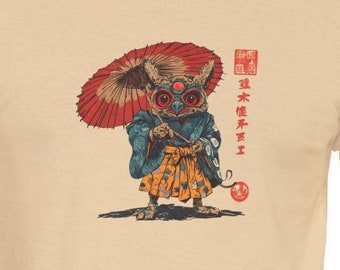 May include: A beige t-shirt with a cartoon illustration of a creature with large eyes and a red umbrella. The creature is wearing a blue and yellow kimono and holding a red ball. The text "真木 暁子" is printed on the shirt.