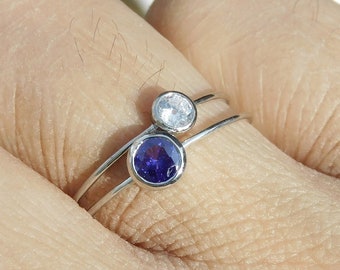 Op de afbeelding: Een zilveren ring met twee kleine edelstenen. De bovenste steen is helder en de onderste steen is paars.