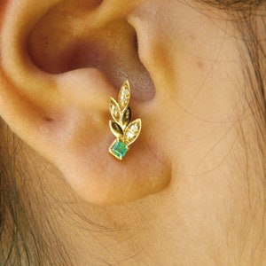 May include: A gold earring with a green emerald stone and small white diamonds set in a leaf design.