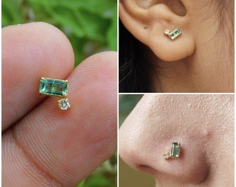 May include: A gold nose ring with a small, rectangular green gemstone and a smaller, round clear gemstone.