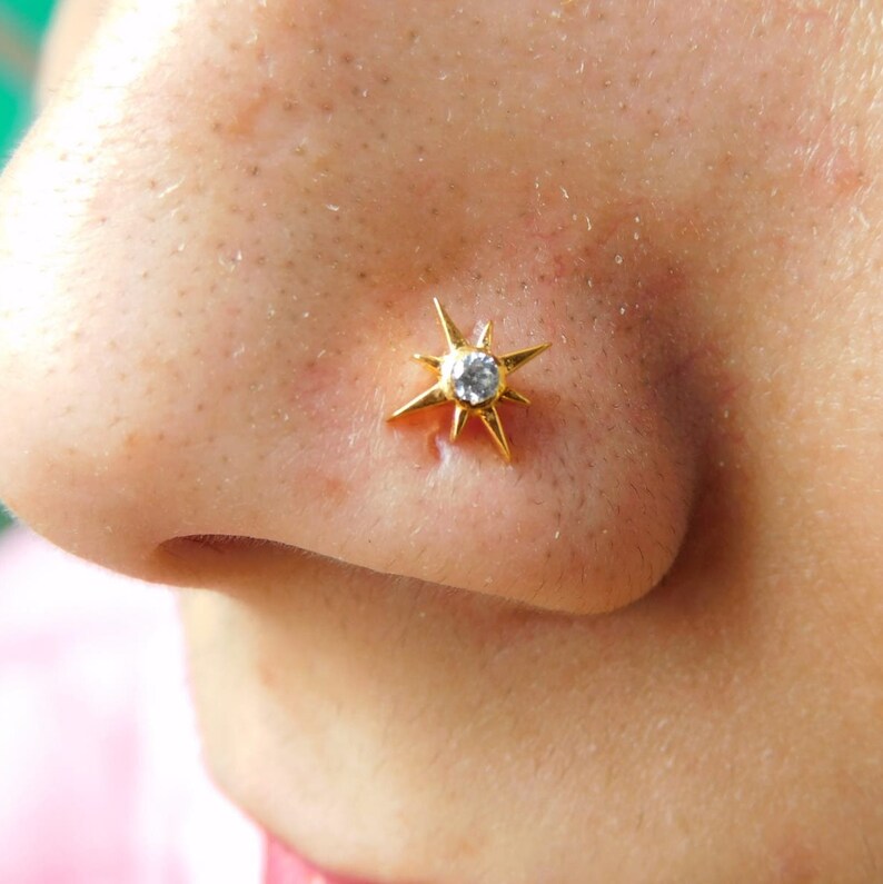 May include: A gold nose ring with a star-shaped design and a clear gemstone in the center.