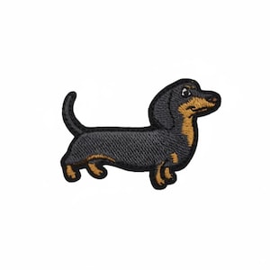 May include: Embroidered patch featuring a black and tan dachshund dog. The patch has a detailed design with a black body, tan accents, and a curved tail. The dog is depicted in a standing position, with its head turned slightly to the side.