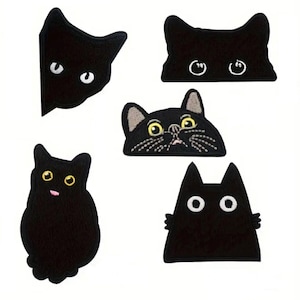 May include: A collection of five black cat-shaped patches with embroidered details. Each patch features a different cat face design, including various eye shapes and expressions. The patches are on a white background.