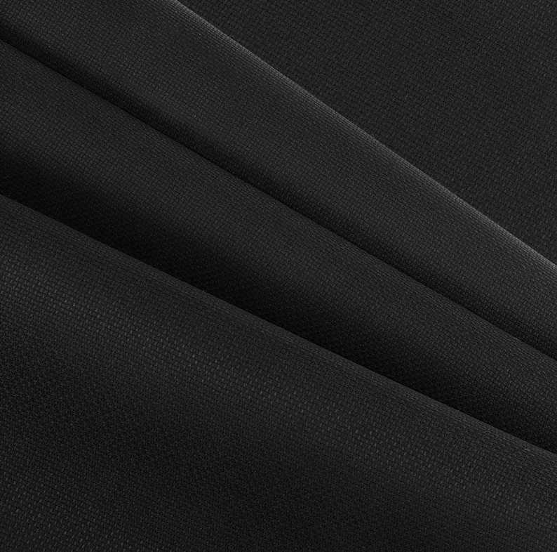 May include: Close-up of black fabric with a subtle textured pattern. The fabric is folded in diagonal lines, creating shadows and highlighting the material's texture. The overall appearance is dark and sleek.
