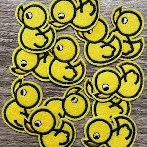 May include: A set of 14 yellow felt iron-on patches featuring a cartoon duck design. The ducks are outlined in black and have a white eye with a black pupil.