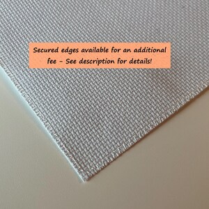 May include: Close-up of a light gray fabric with a textured weave. The edges are neatly stitched. An orange rectangle with the text "Secured edges available for an additional fee - See description for details!" is visible.