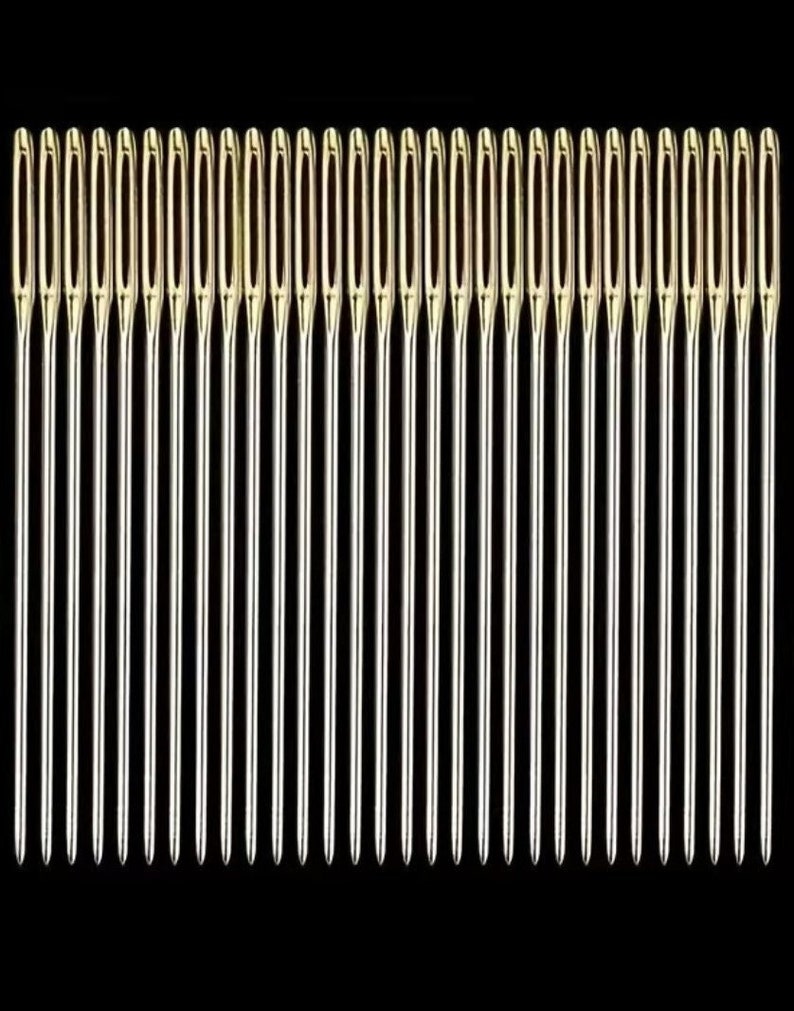May include: A set of 30 silver sewing needles with gold eye tips, arranged in a row against a black background.