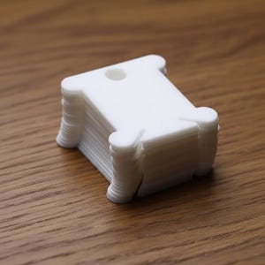 May include: A stack of white plastic bobbins, each with a spool-like shape and a small hole at the top. The bobbins are neatly stacked on a wooden surface, suggesting a craft or sewing theme.