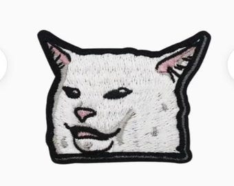 May include: Embroidered patch featuring the meme of a white cat with a smug expression. The cat's face is detailed with black eyes, a pink nose, and a slightly open mouth. The patch has a black border, suitable for application on clothing or accessories.