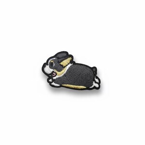 May include: Embroidered patch featuring a cartoon rabbit in a running pose. The patch has a black body with white and yellow accents, and a white outline. The rabbit's face is white with black eyes and a pink tongue.