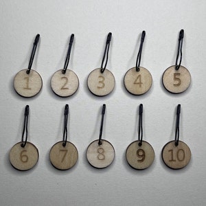May include: Ten wooden tags with black string loops, each with a number from 1 to 10 printed on them.