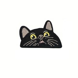 May include: Black cat patch with embroidered details. The cat has yellow eyes, a pink nose, and white whiskers. The ears are gray. The patch is a fun accessory for clothing, bags, or other fabric items.