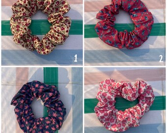 May include: Four floral patterned scrunchies in different colors and patterns. The scrunchies are made of fabric and have a gathered look.