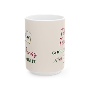 May include: A cream-colored ceramic mug featuring Mahjong tile illustrations, red and green text that reads Tile Tea, Jongg Night, and GOOD COMPANY, along with a small floral graphic and a single Mahjong tile icon on the side.
