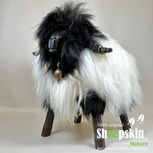 May include: A decorative sheep-shaped stool with a black and white faux fur body. The sheep has a black metal face and horns, with a small bell hanging from its neck. The stool has dark wooden legs and the text "100% original Sheepskin" is visible.
