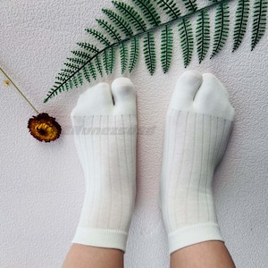 May include: A pair of white ribbed socks with split toes. The socks are on a person's feet, and the toes are separated.
