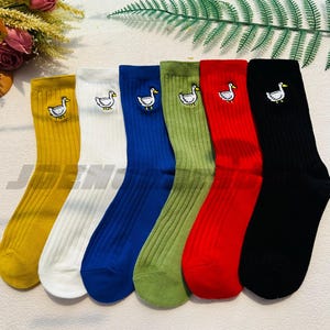 May include: Set of six pairs of colourful socks with a white embroidered duck design. The socks are ribbed and come in yellow, white, blue, green, red, and black.